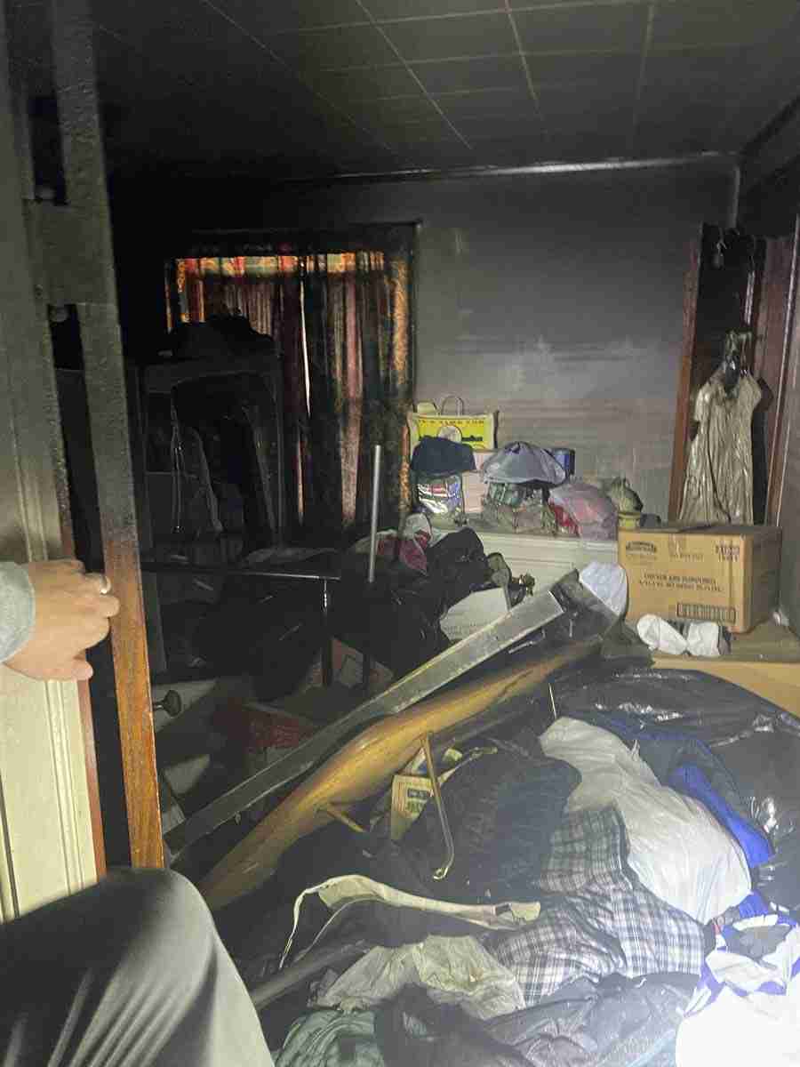 Cluttered room with boxes, clothes, and furniture.